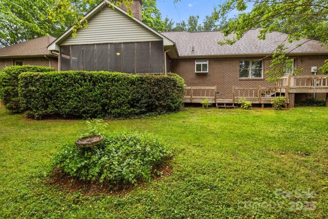 rear view of property featuring a wooden deck, roof with shingles, a chimney, brick siding, and a yard