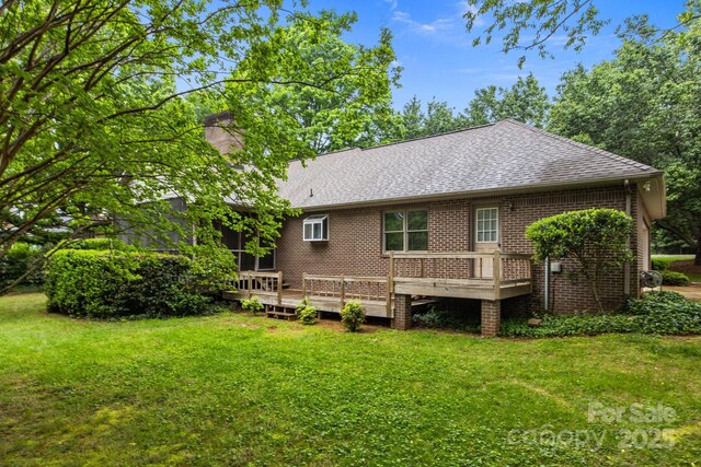 rear view of property with a lawn, a deck, a shingled roof, and brick siding