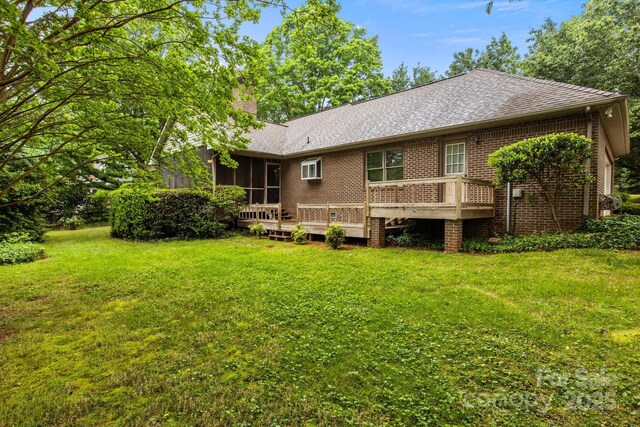 rear view of property with a deck, roof with shingles, a chimney, a sunroom, and a lawn