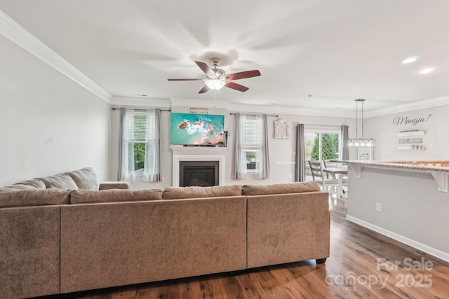 living area with a ceiling fan, a healthy amount of sunlight, dark wood-style flooring, and a glass covered fireplace