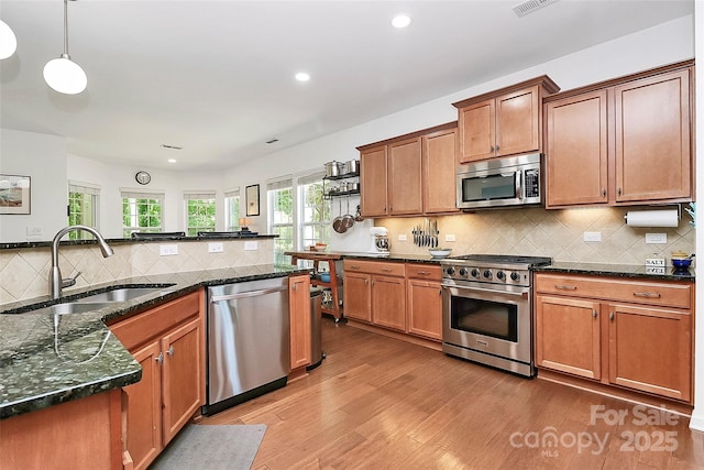 kitchen featuring appliances with stainless steel finishes, a sink, light wood finished floors, recessed lighting, and backsplash