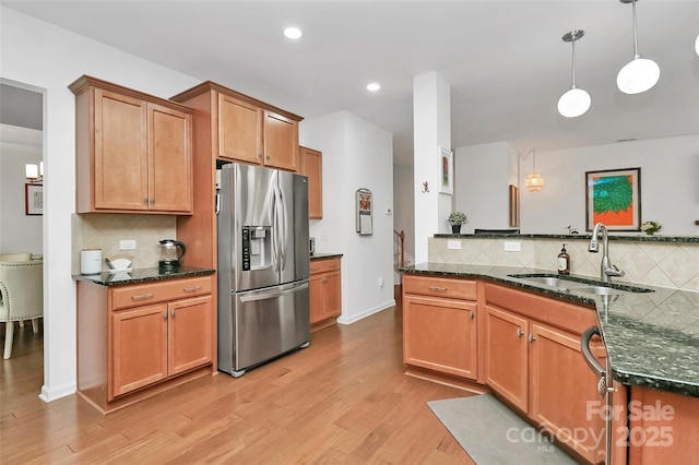 kitchen with decorative backsplash, stainless steel refrigerator with ice dispenser, a sink, light wood finished floors, and hanging light fixtures