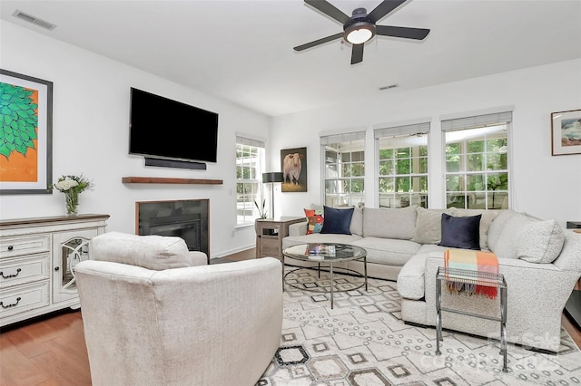 living room featuring visible vents, a glass covered fireplace, wood finished floors, a healthy amount of sunlight, and ceiling fan