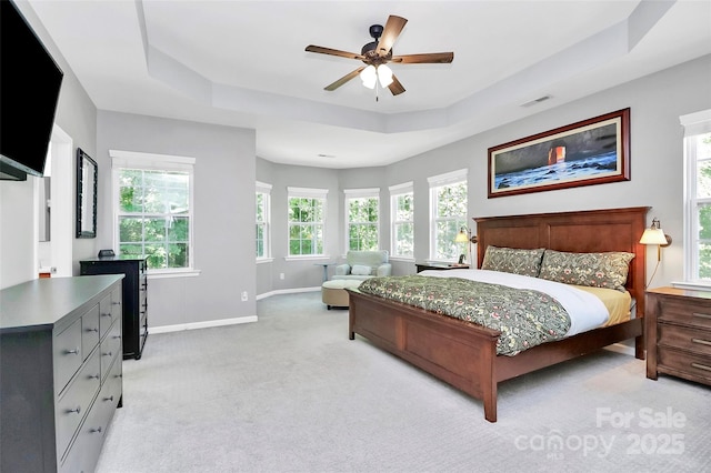 bedroom with multiple windows, baseboards, light carpet, and a raised ceiling