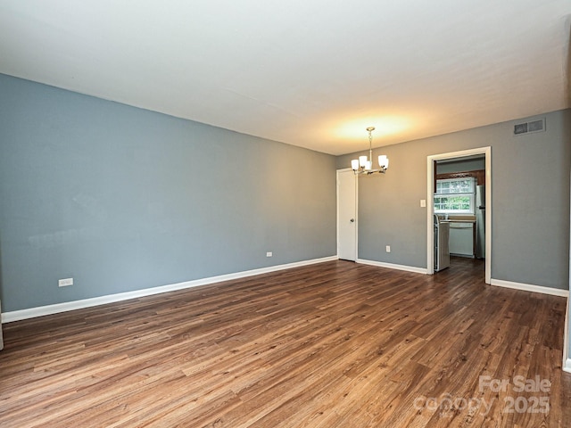 spare room with a chandelier, baseboards, visible vents, and wood finished floors