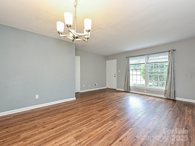 unfurnished room with an inviting chandelier, baseboards, and wood finished floors