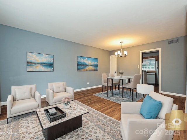 living room featuring visible vents, baseboards, wood finished floors, and an inviting chandelier