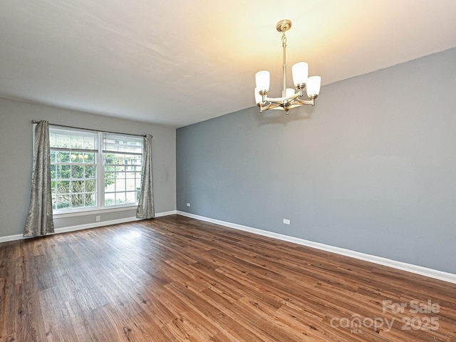 unfurnished room featuring an inviting chandelier, baseboards, and dark wood-style floors