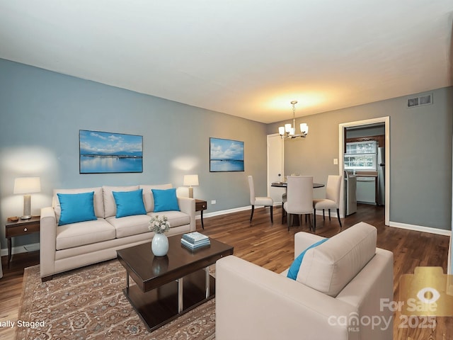 living area featuring a chandelier, baseboards, visible vents, and wood finished floors