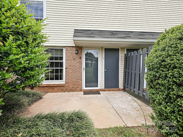 view of exterior entry featuring brick siding and a patio