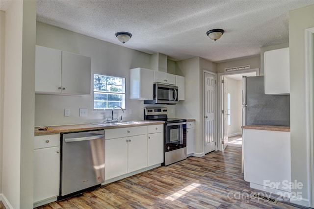 kitchen with wood finished floors, appliances with stainless steel finishes, light countertops, white cabinets, and a sink