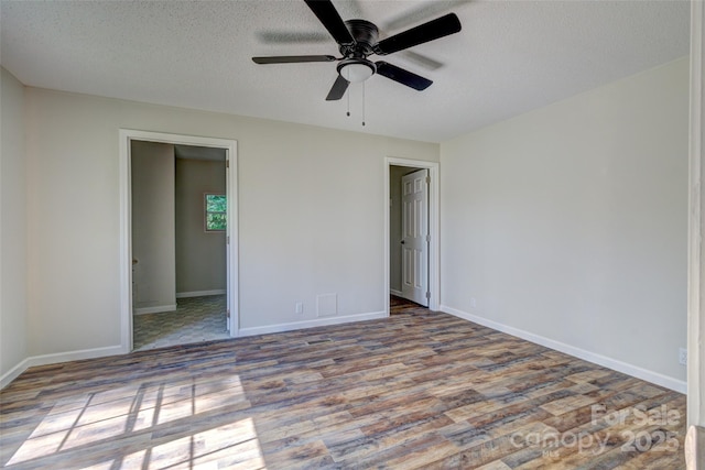 unfurnished bedroom featuring a textured ceiling, baseboards, wood finished floors, a ceiling fan, and a walk in closet