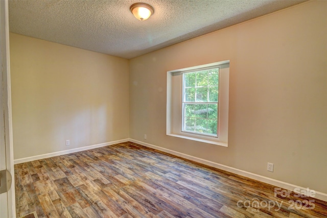 empty room with a textured ceiling, wood finished floors, and baseboards