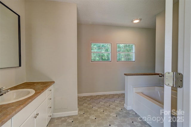 bathroom with baseboards, a garden tub, a textured ceiling, and vanity