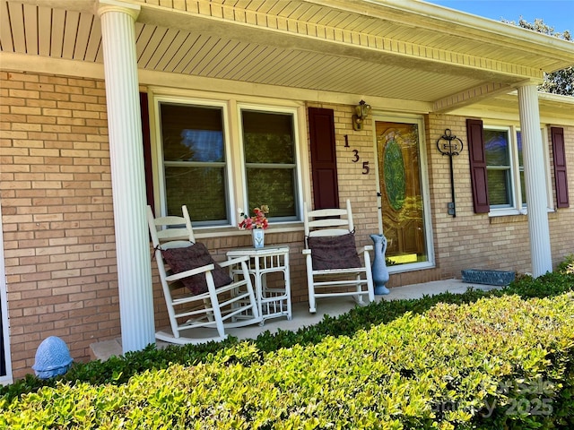doorway to property with a porch and brick siding