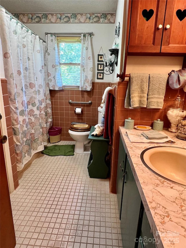 full bath featuring vanity, toilet, tile walls, a wainscoted wall, and tile patterned floors