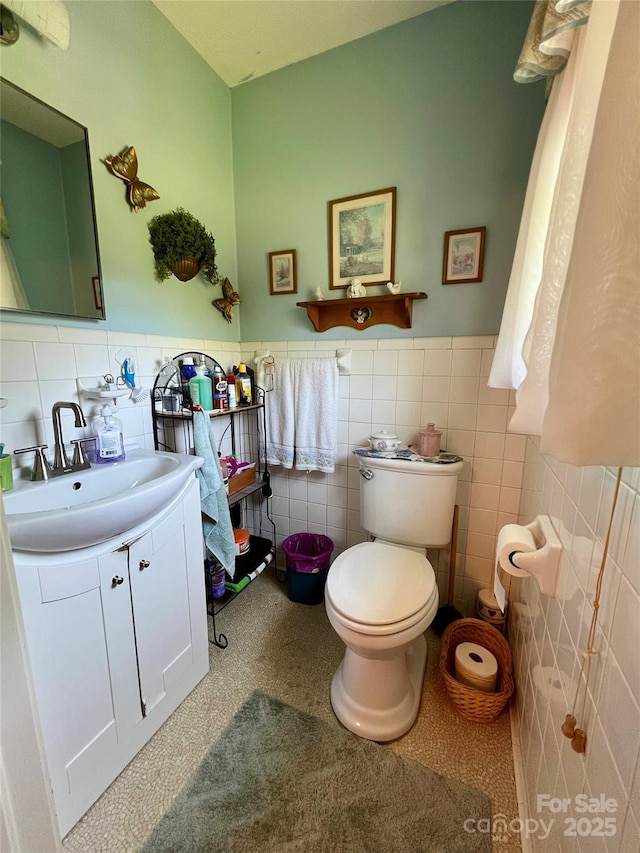 bathroom with tile walls, a wainscoted wall, vanity, and toilet