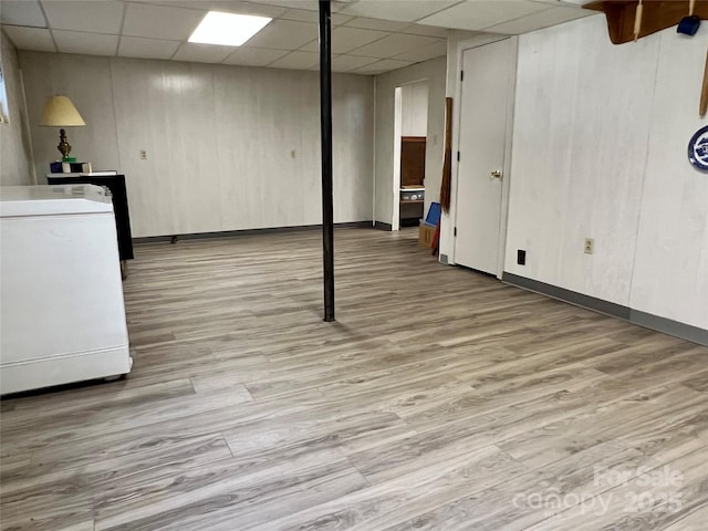 finished basement featuring light wood-style floors, baseboards, and a drop ceiling