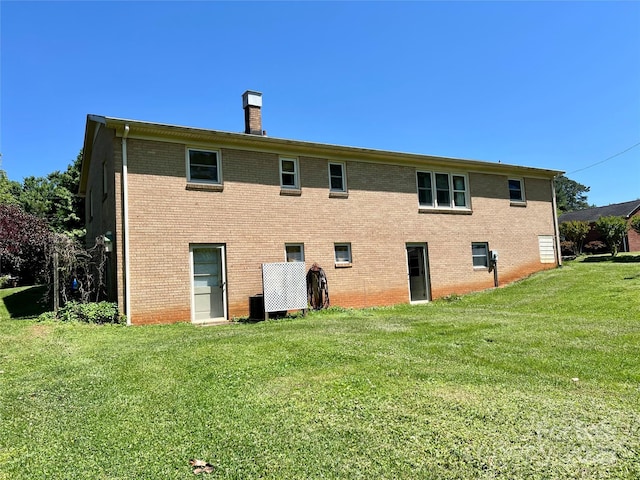 back of property featuring a lawn, brick siding, and a chimney