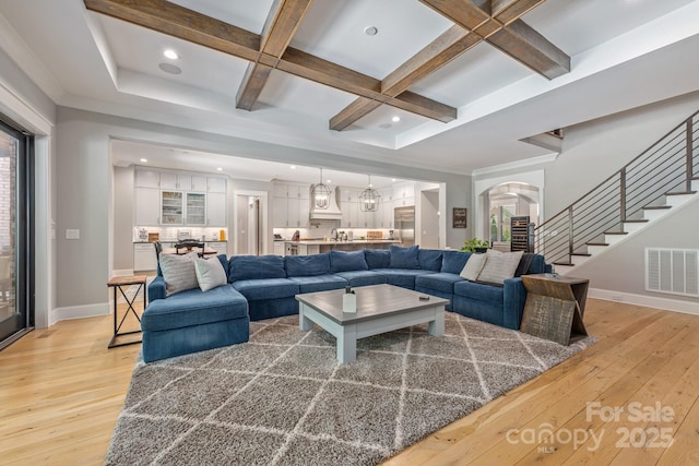 living area with coffered ceiling, visible vents, baseboards, and light wood-style floors