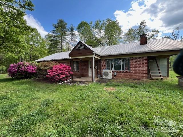 back of house featuring a chimney, brick siding, metal roof, and ac unit