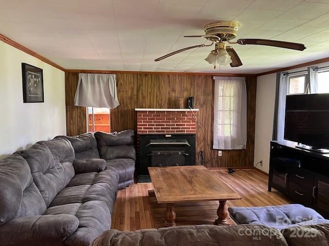 living room featuring ornamental molding, a ceiling fan, wood walls, and light wood-style flooring