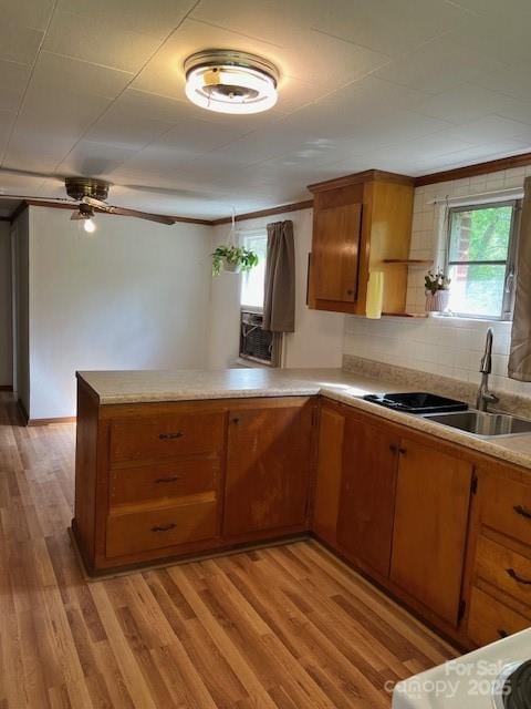 kitchen featuring a sink, brown cabinets, light wood-type flooring, a peninsula, and light countertops