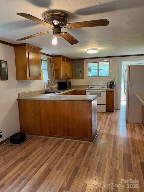 kitchen with white appliances, a sink, light wood-style floors, a peninsula, and brown cabinetry