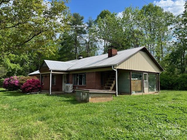 rear view of property with a chimney, metal roof, a yard, and ac unit