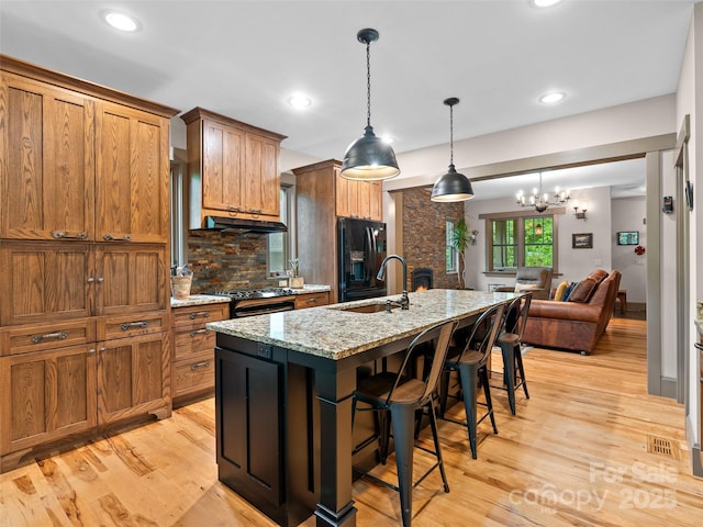 29 Ravenna St, Asheville, NC 28803 - kitchen with black fridge with ice dispenser, brown cabinetry, tasteful backsplash, a sink, and a kitchen island with sink
