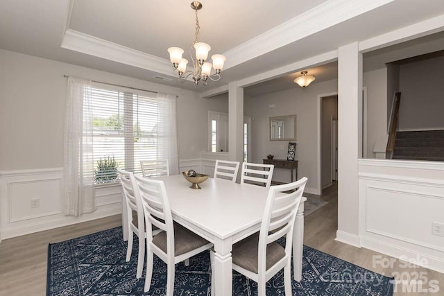 dining room featuring wood finished floors, an inviting chandelier, a wainscoted wall, crown molding, and a tray ceiling
