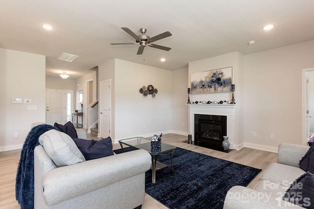 living room with light wood-style floors, baseboards, visible vents, a ceiling fan, and a fireplace with flush hearth