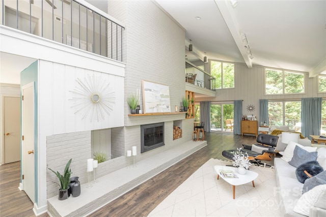 living area with wood finished floors, high vaulted ceiling, beamed ceiling, and a brick fireplace