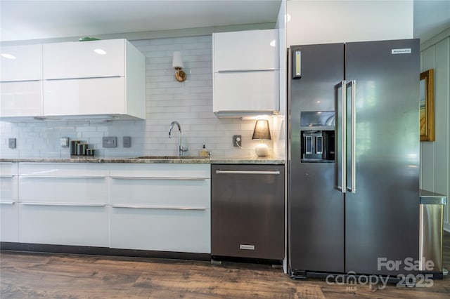 kitchen with light stone counters, white cabinetry, stainless steel appliances, and a sink