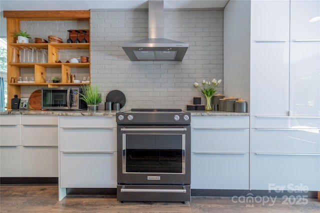 kitchen with wall chimney range hood, light stone counters, white cabinetry, stainless steel appliances, and wood finished floors