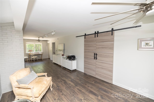 sitting room featuring track lighting, a barn door, a ceiling fan, and dark wood-style floors