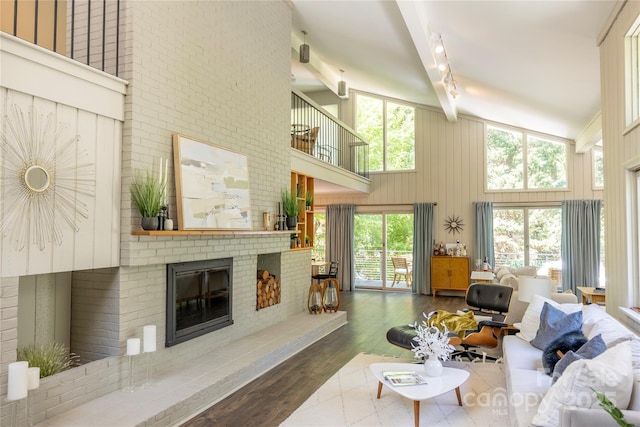living room featuring rail lighting, wood finished floors, high vaulted ceiling, and a brick fireplace