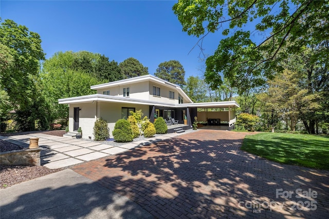 view of front facade featuring decorative driveway, a porch, a front yard, and an attached carport