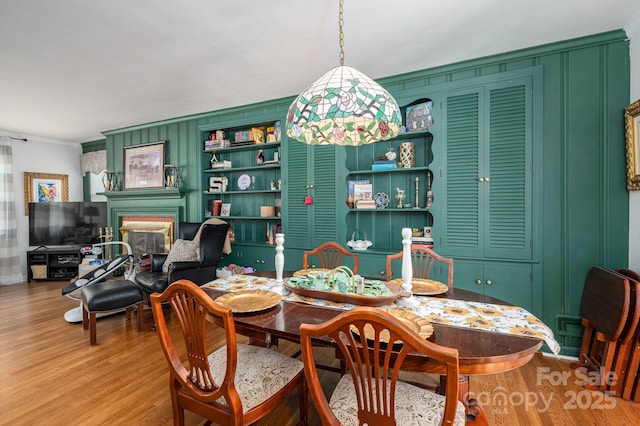 dining space featuring a glass covered fireplace, crown molding, and light wood-style floors