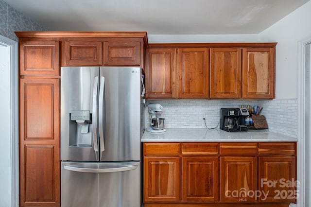 kitchen with light countertops, stainless steel refrigerator with ice dispenser, brown cabinetry, and decorative backsplash