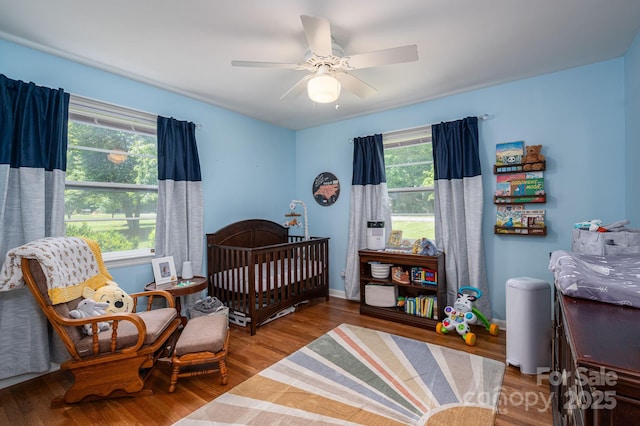 bedroom featuring a ceiling fan, a crib, and wood finished floors