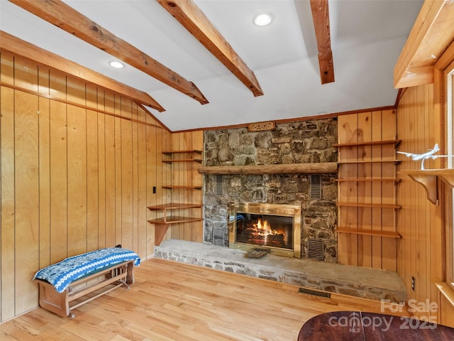 unfurnished room with lofted ceiling with beams, wood walls, a stone fireplace, and wood finished floors