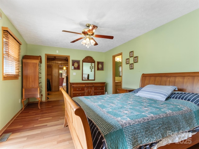 bedroom featuring ensuite bath, light wood-style floors, a textured ceiling, a ceiling fan, and visible vents