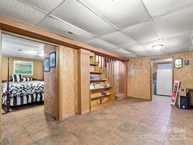 finished basement with visible vents, freestanding refrigerator, and a paneled ceiling