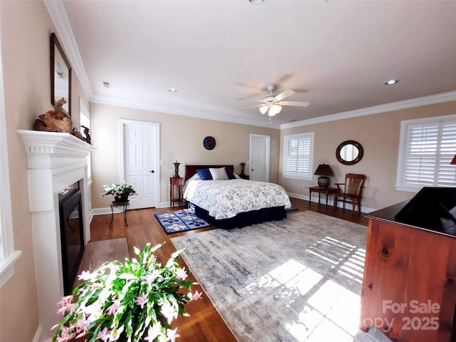 bedroom featuring wood finished floors, a glass covered fireplace, baseboards, visible vents, and crown molding