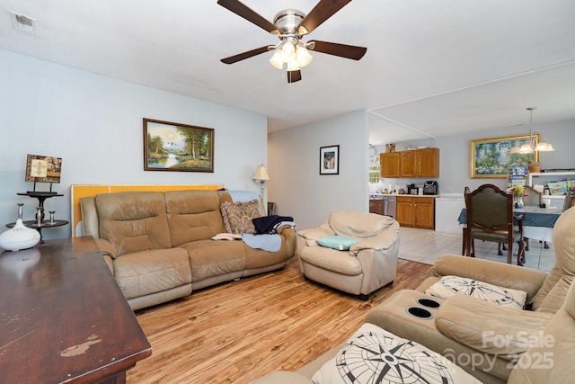 living room with a ceiling fan, light wood finished floors, and visible vents