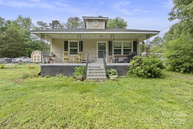 view of front facade featuring covered porch, a storage unit, fence, a front lawn, and stairs