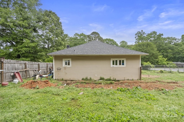 view of side of property featuring a yard, a fenced backyard, and roof with shingles