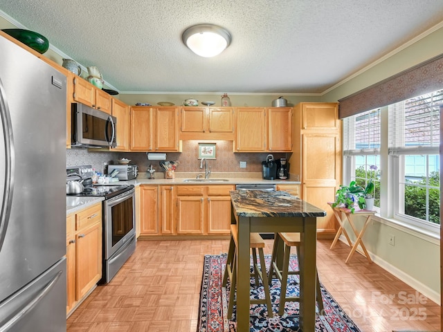 kitchen featuring a textured ceiling, light brown cabinets, stainless steel appliances, and a sink