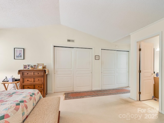 bedroom featuring visible vents, vaulted ceiling, light carpet, a textured ceiling, and multiple closets